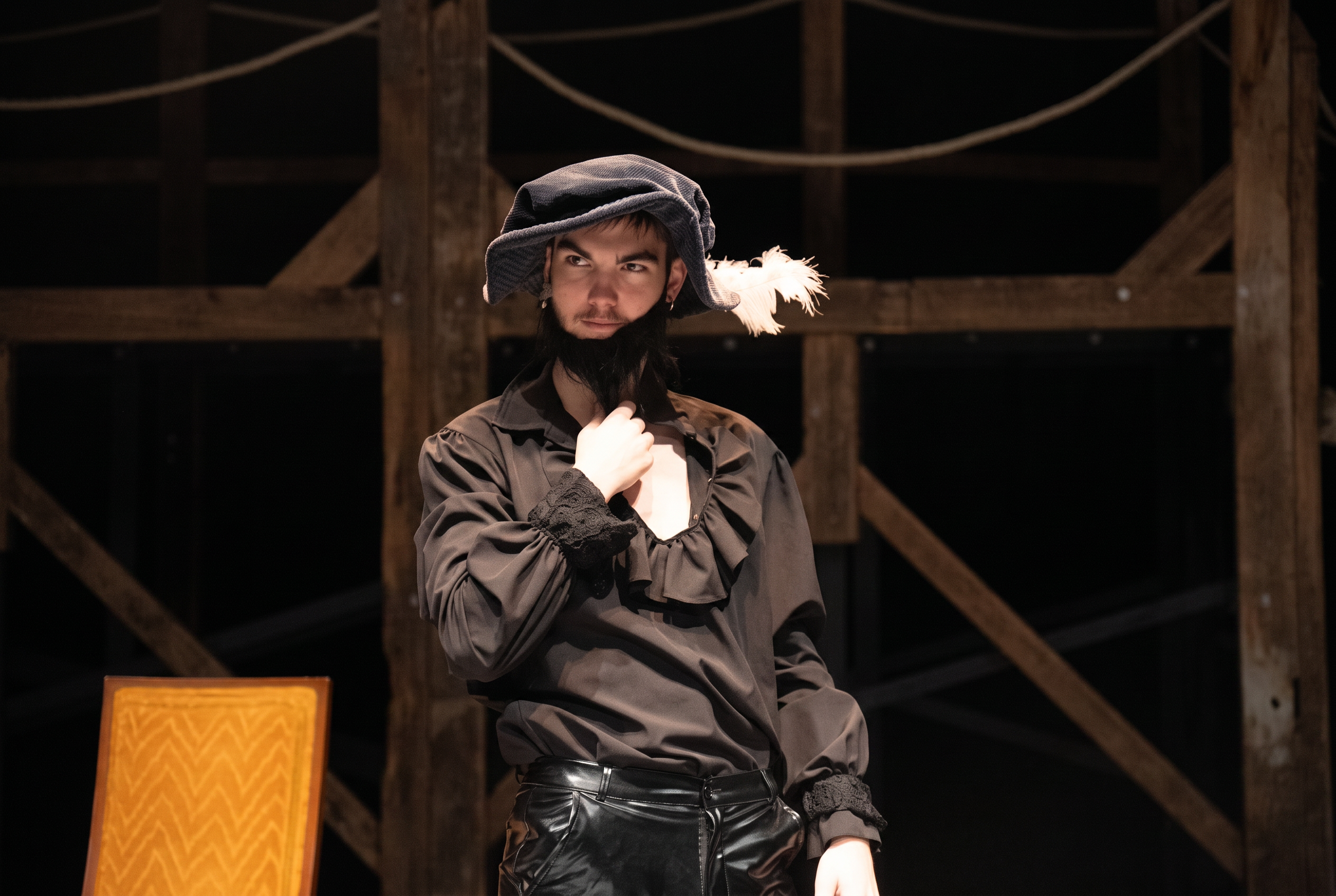 Richard Jordan in period costume with a feathered cap on a dimly lit wooden stage set